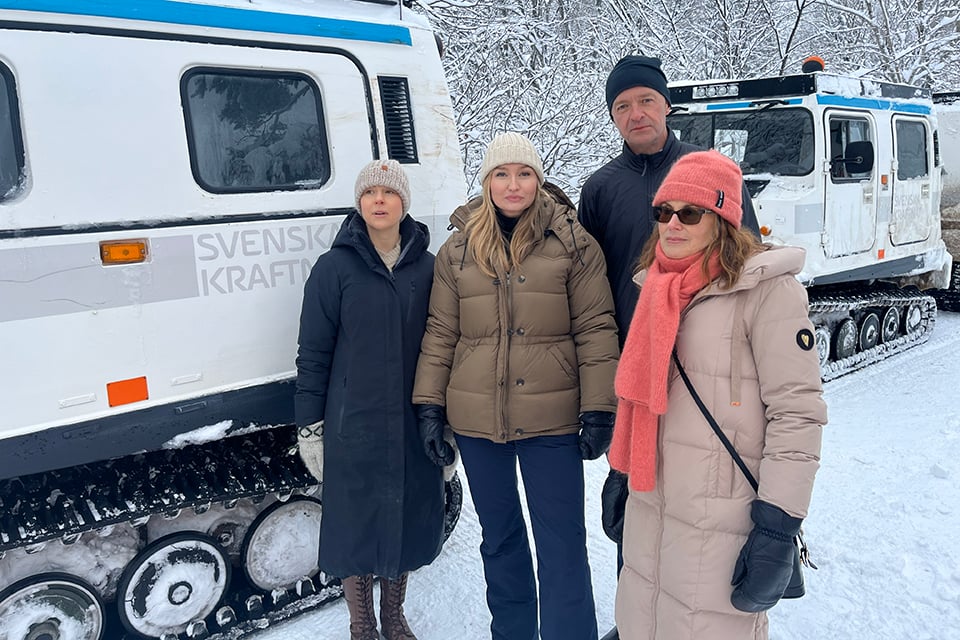 Fyra personer framför en vit bandvagn i ett snöigt landskap
