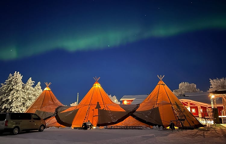 Norrsken på en mörkblå himmel över tre upplysta tält