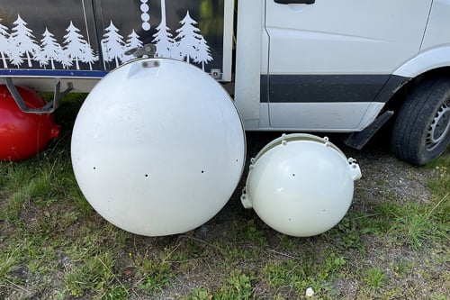 Bilden föreställer ett gammalt och nytt klot som hängs upp på kraftledningen som flyghindermarkering. Kloten ligger bredvid varandra på marken när bilden tas. Det gamla klotet är större än det nya klotet, som är mindre. Båda kloten är vita och gjorda i tålig plast. Det stora klotet väger 30 kilo och det nya klotet väger 6 kilo.