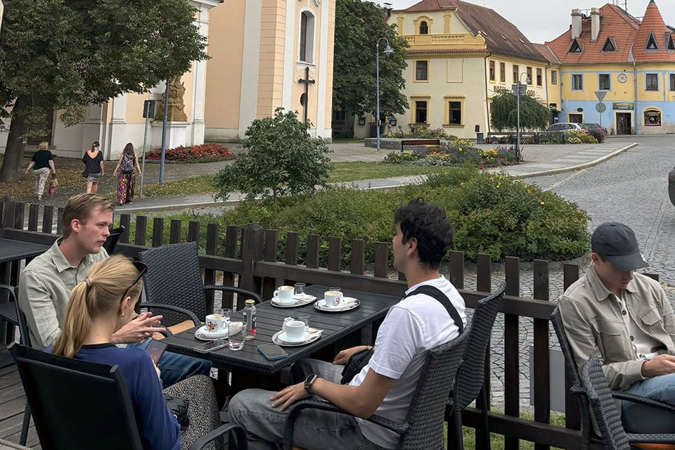 Tre traineer sitter runt ett bord på en uteservering och fikar