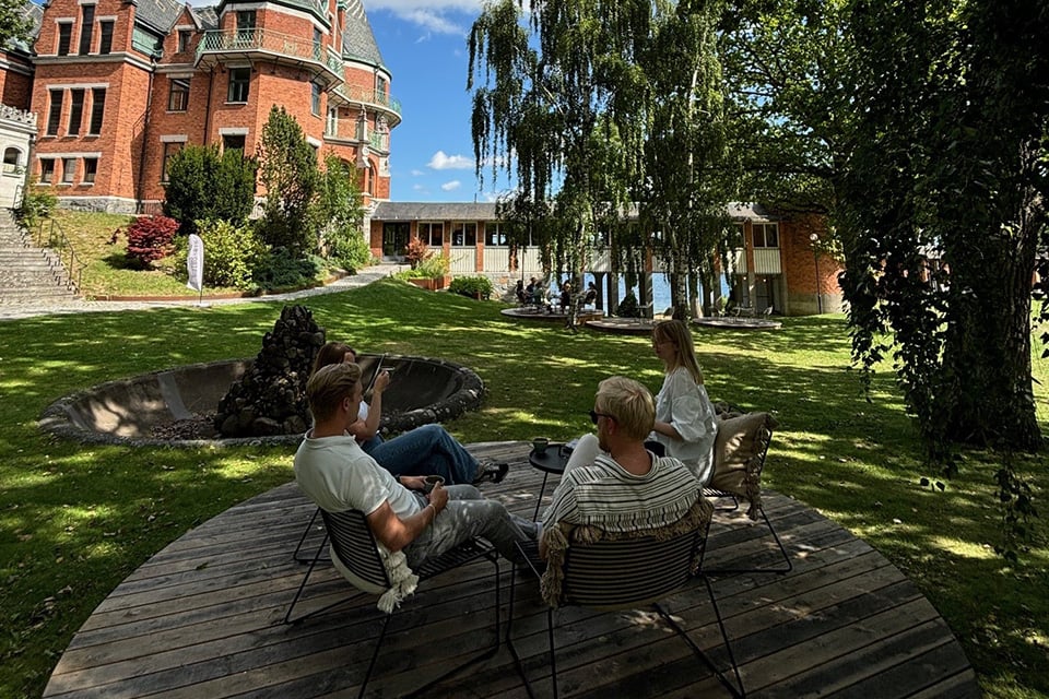 Fyra traineer sitter vid bord i kursgårds trädgård.