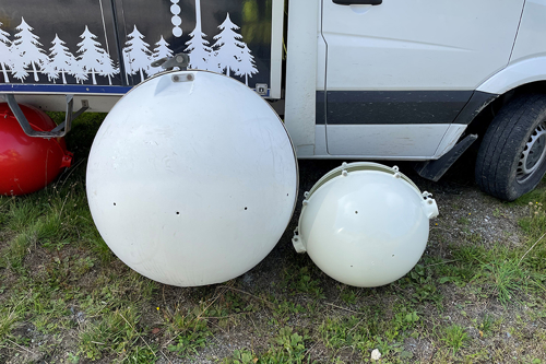 Bilden föreställer ett gammalt och nytt klot som hängs upp på kraftledningen som flyghindermarkering. Kloten ligger bredvid varandra på marken när bilden tas. Det gamla klotet är större än det nya klotet, som är mindre. Båda kloten är vita och gjorda i tålig plast. Det stora klotet väger 30 kilo och det nya klotet väger 6 kilo.