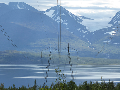 Bild på anslutande kraftledning till station Ritsem. I bakgrunden syns blå berg och vatten.