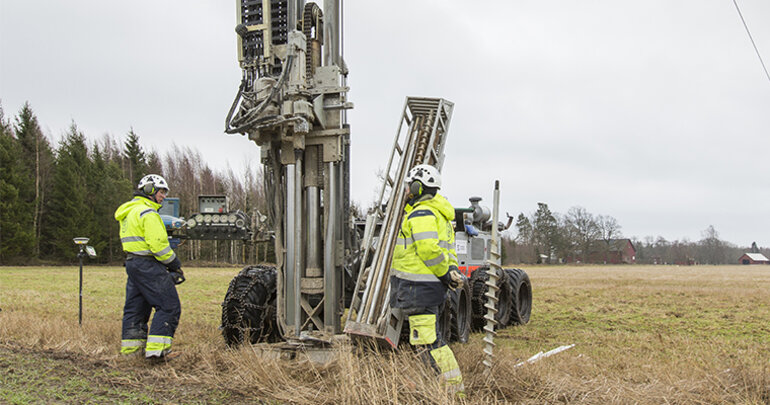 Två män i arbetskläder vid en  borrbandvagn