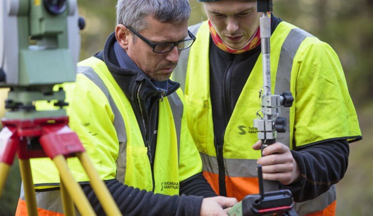 Bild på två män i arbetarkläder som studerar mätvärden från ett instrument