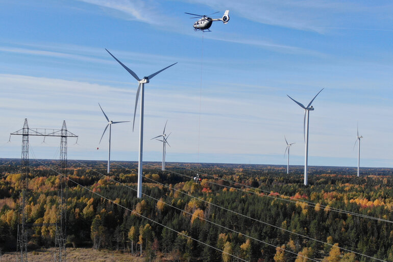 Montörer hänger i vajer under helikopter vid högspänningsledning