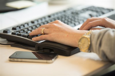 Bilden visar en hand i närbild som skriver på ett tangentbord till en dator.