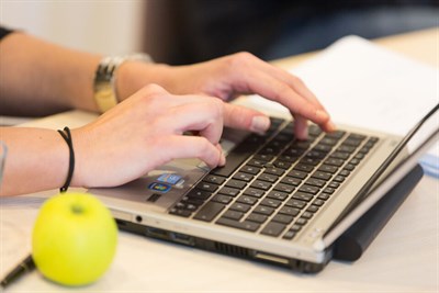 Händer som skriver på en laptop med ett äpple i förgrunden.