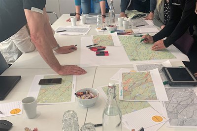 Bild på ett bord på kartor uppslagna. Människor pekar med händer och pennor över materialet. Det är tydligt att samtal pågår om innehållet i kartorna.