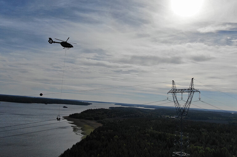 Helikopter flyger över ledning där personer arbetar