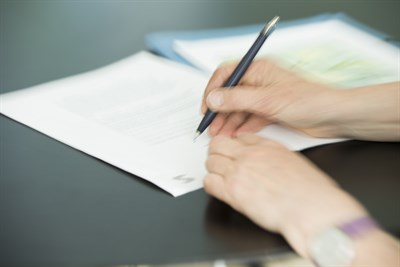 Hand som signerar ett papper som ligger på ett bord.