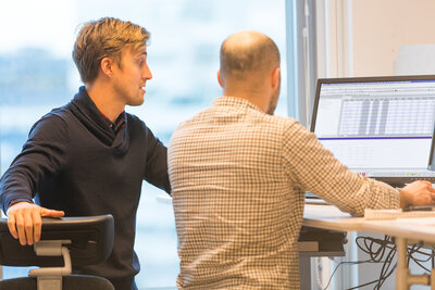 Två personer står och tittar och pekar på en datorskärm