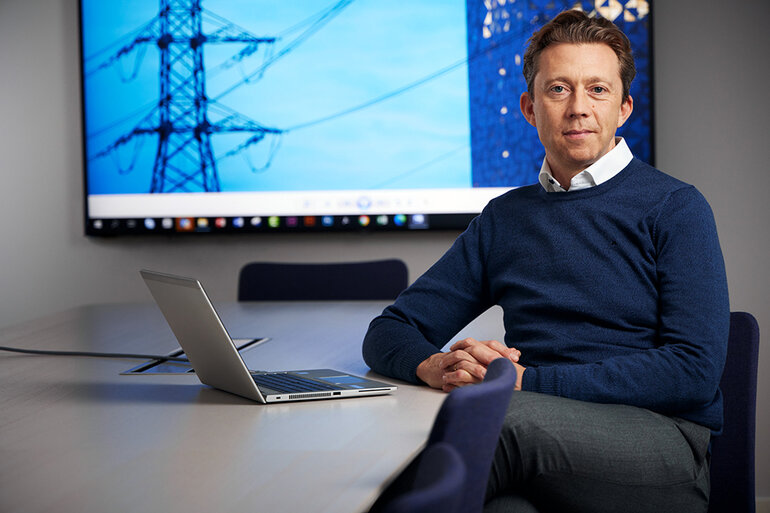 Driftchefen sitter vid ett bord med en skärm i bakgrunden