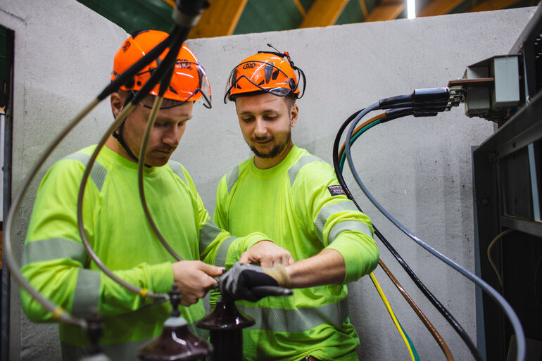 Två män i varselkläder som lagar en elkabel