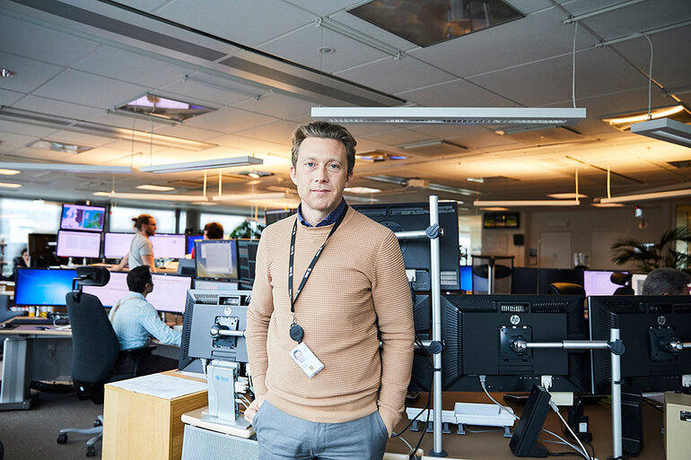 Driftchefen står i ett kontrollrum bland många skärmar och människor som arbetar