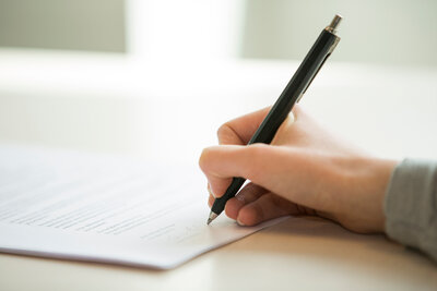 Penna i hand som vilar på papper.