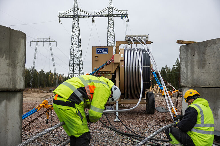 Två personer i varselkläder arbetar med en lina som ska upp i en kraftledning.