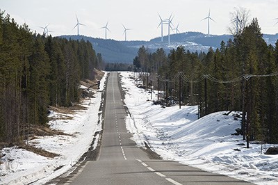 Väg genom vinterlandskap med vindkraftverk i bakgrunden