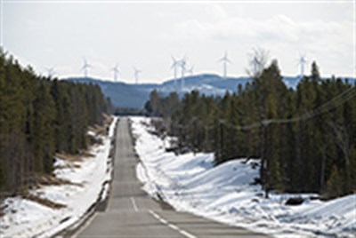Väg i vinterlandskap med vindkraftverk i bakgrunden